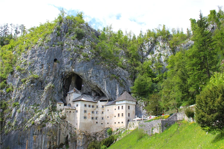 Hrad Predjama vestavěný do skalního útesu obklopeného lesem, Slovinsko | Slovinsko křížem krážem