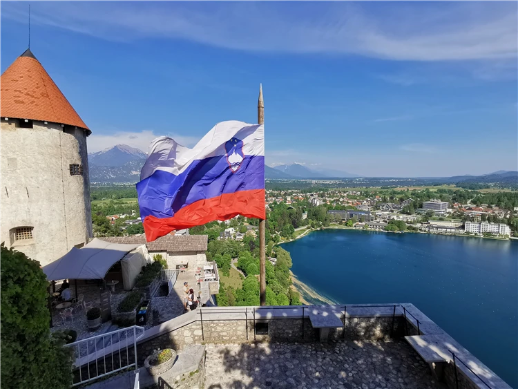 Slovinská vlajka vlající z hradu Bled s výhledem na jezero a Alpy | Slovinsko křížem krážem