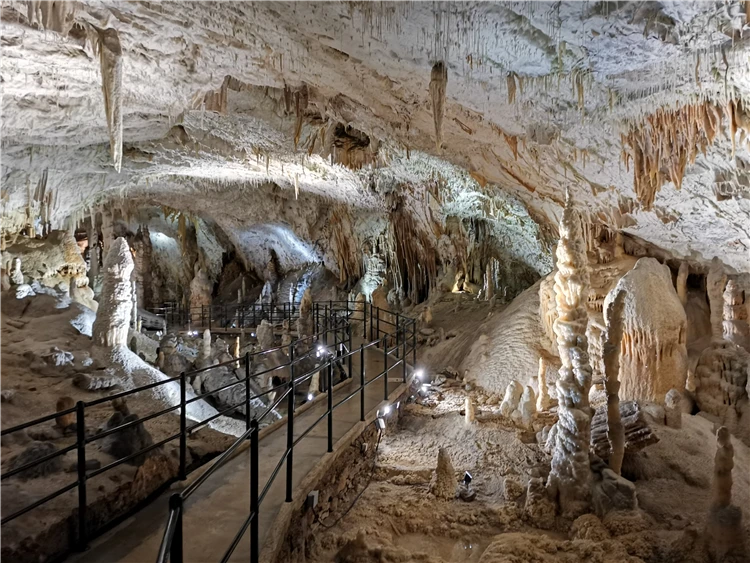 Osvětlený jeskynní dóm se stalaktity, stalagmity a turistickou stezkou s zábradlím. | Slovinsko křížem krážem