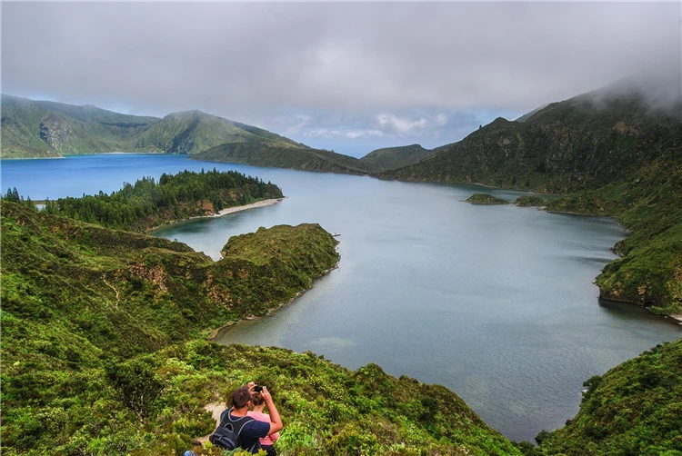 Výhled na jezero Lagoa do Fogo v sopečném kráteri na Azorách, turisté fotí scenérii. | Azorské ostrovy São Miguel a Santa Maria