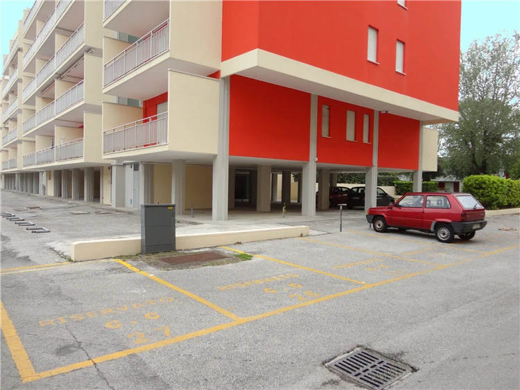 Parkoviště před moderním hotelovým komplexem s červenou fasádou, Itálie | Caorle - Porto Santa Margherita / Residence Acapulco